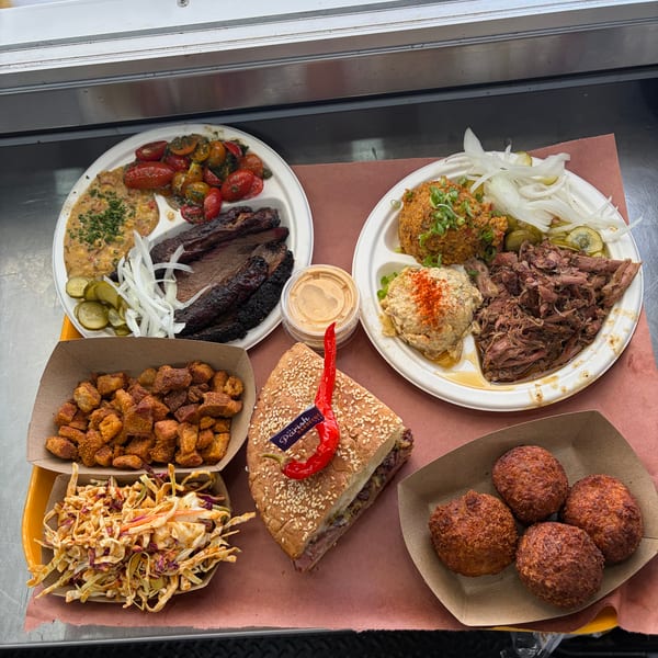 A tray of barbecue food including brisket, pulled pork, sides, and a sandwich with a red pepper.