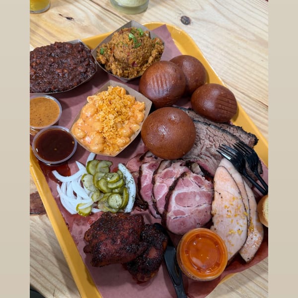 A large platter of Parish Barbecue's smoked meats, sides, and sauces on a wooden table.