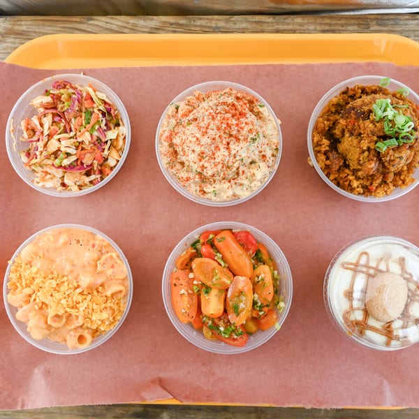 Six plastic containers of various side dishes, including coleslaw, macaroni salad, and dessert.